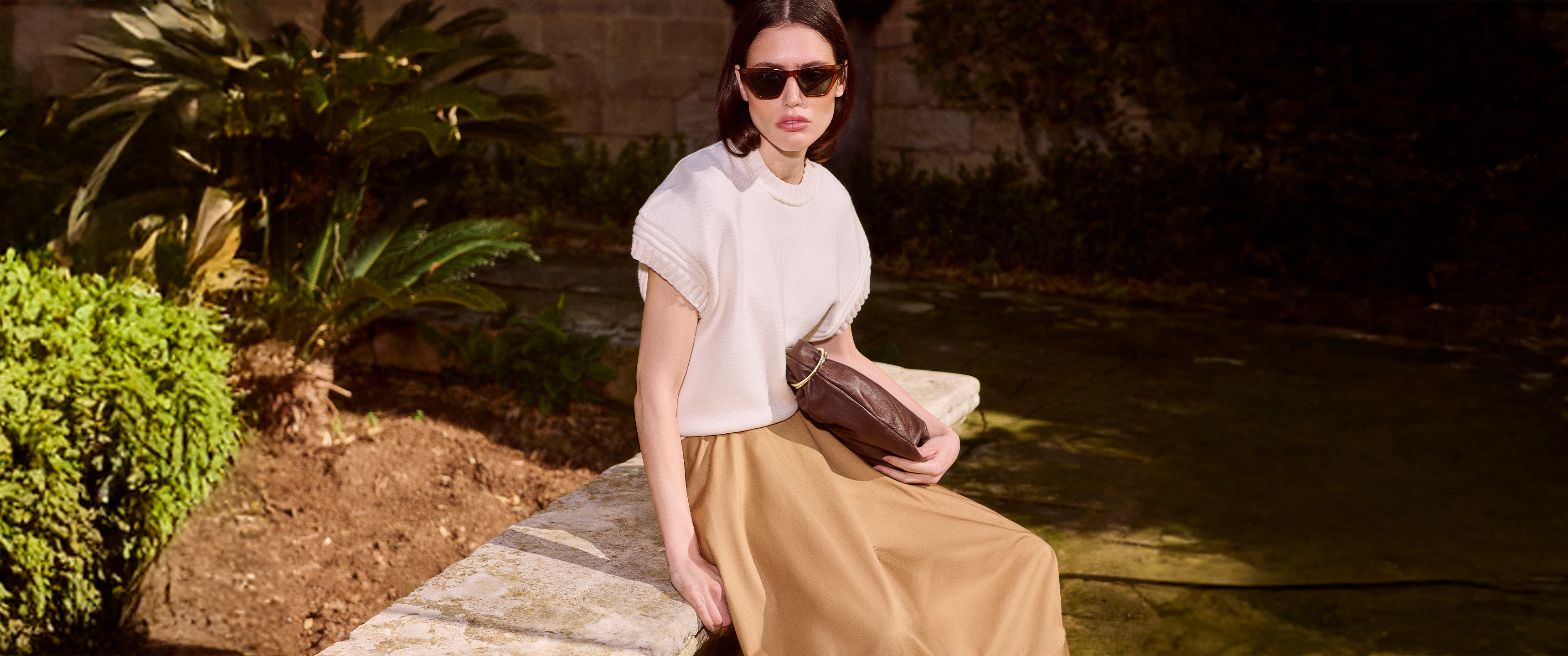 Model wearing a gold satin skirt, white top and sunglasses holding a bag sold at Karen Millen for Karen Millen discount codes