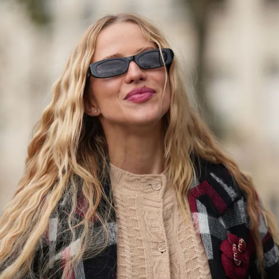 Woman with long blonde, wavy hair walks down the road during fashion week in a tartan jacke t