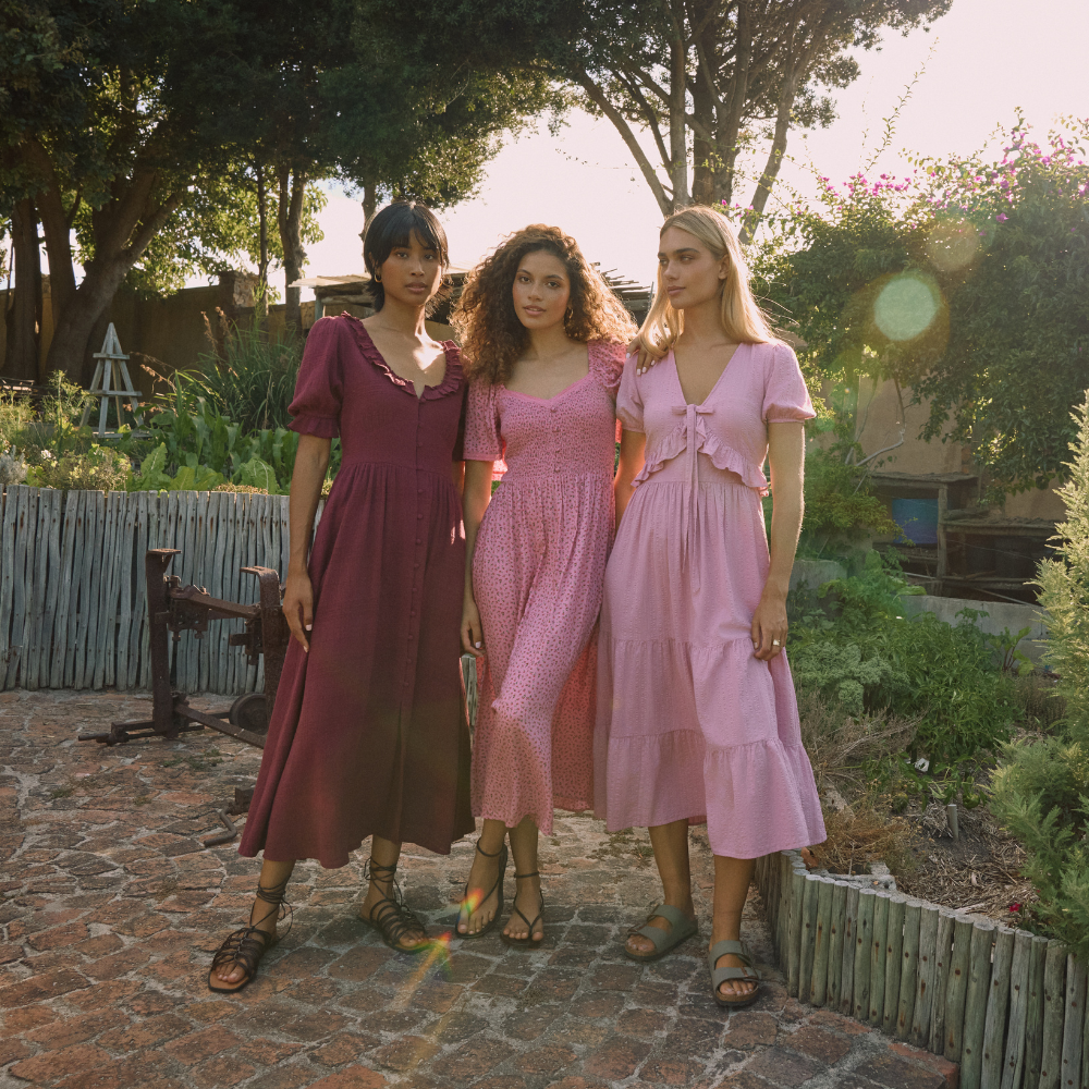 three models wearing nobody's child spring/summer dresses in shades of pink in a city garden